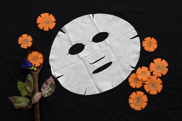 Naturkosmetik Kräuter Aroma Blatt Maske Gesundheit auf der Haut Gesichtsextrakt aus Karotten Essenz Gesichtsmaske Dekoration flach legen Stil auf Hintergrund schwarz - Foto, Bild