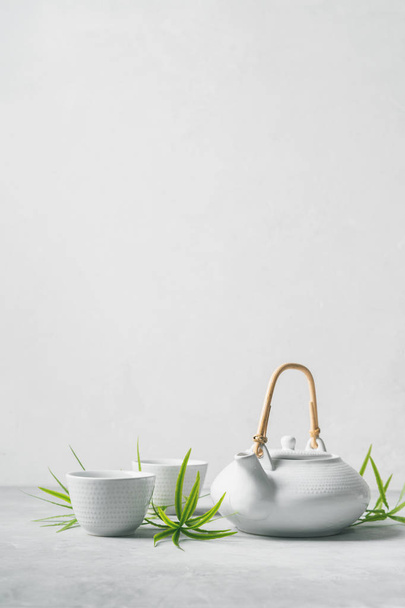 Asian set with green tea, cups and teapot with bamboo leaves on grey background  - 写真・画像