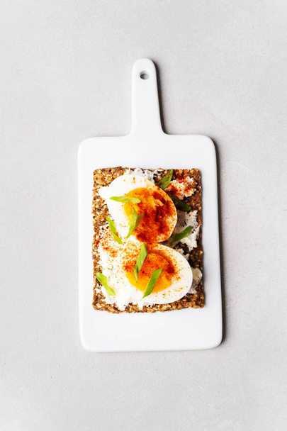 Top view of Superfood protein toast with delicious toppings on top: boiled eggs with onion and paprika on cream cheese lie on ceramic white board. - 写真・画像