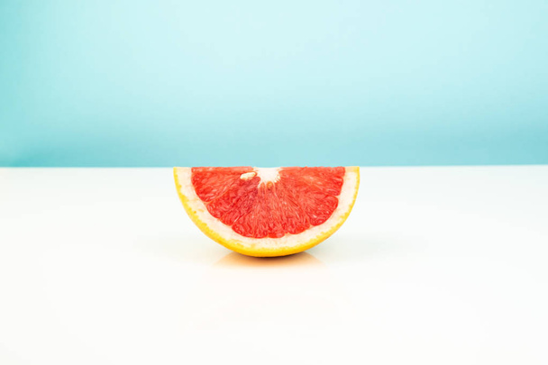 Half of grapefruit on white and blue background. Minimalistic image of slice of citrus at sparse bright environment. - Фото, зображення