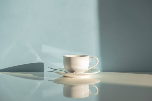 Cup of steaming coffee on seafoam green background in natural sunlight. Abstract photo of hot espresso drink on pale blue-green table and wall - Φωτογραφία, εικόνα