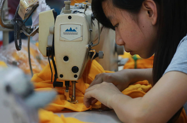 A female Chinese worker sews clothes to be exported to the United States and Europe at Jiujiang Rongda Garment Factory in Jiujiang city, east Chinas Jiangxi province, 20 May 2013 - Fotoğraf, Görsel