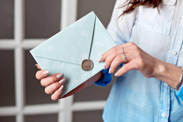 Close-up of a woman with a slim body holding a blue rectangular invitation card in an envelope of a card. - Zdjęcie, obraz