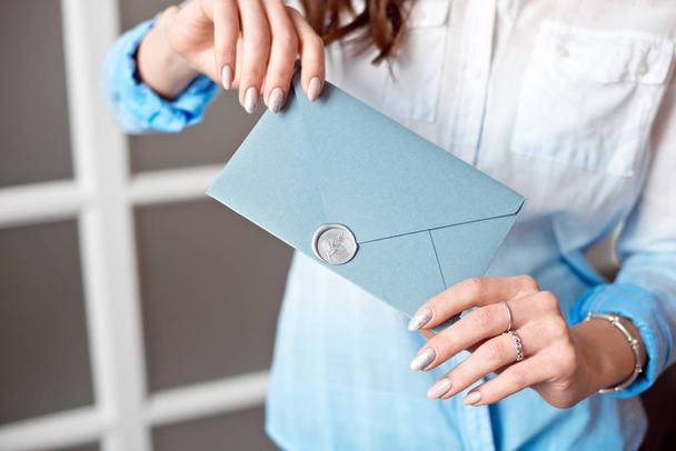 Крупный план молодой девушки с голубым прямоугольным подарочным конвертом с приглашениями, товарами и картой обслуживания
. - Фото, изображение
