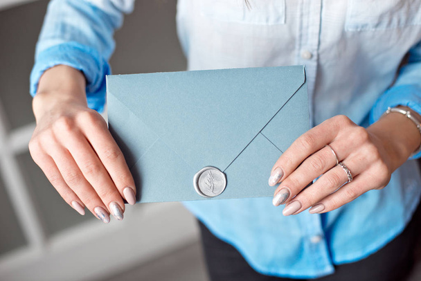 Primer plano de una joven sosteniendo un sobre de regalo rectangular azul con invitaciones, productos y servicios tarjeta
. - Foto, Imagen