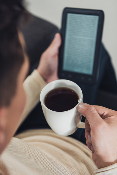 selective focus of cup with drink in hand of man reading ebook  - 写真・画像