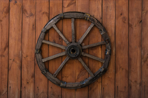 ein altes hölzernes Wagenrad, das an einem lackierten Holzzaun hängt - Foto, Bild