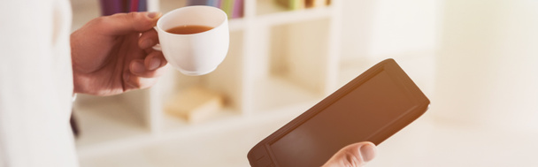 обрізаний вид електронного читання і чашка чаю в руках людини
  - Фото, зображення