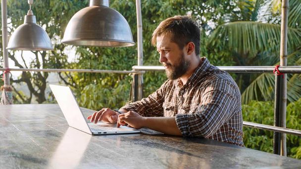 Красивий бородатий чоловік друкує на ноутбуці на відкритому повітрі
 - Фото, зображення
