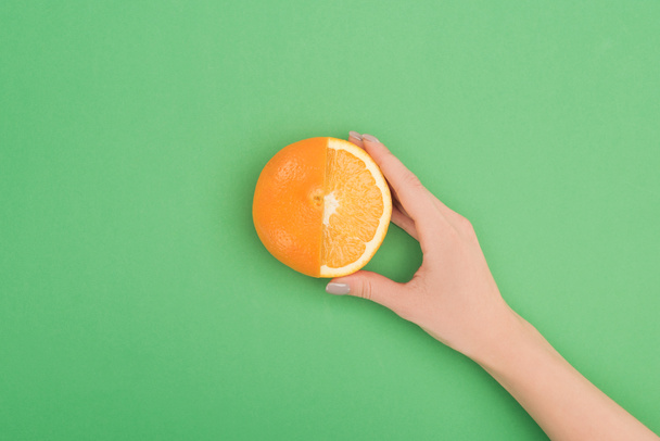 cropped view of female hand with fresh partially cut orange on green background - 写真・画像