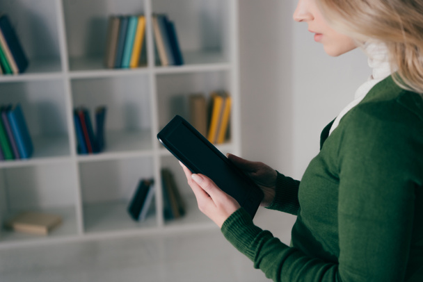 bijgesneden beeld van vrouw met e-reader in de buurt van boekenplank - Foto, afbeelding