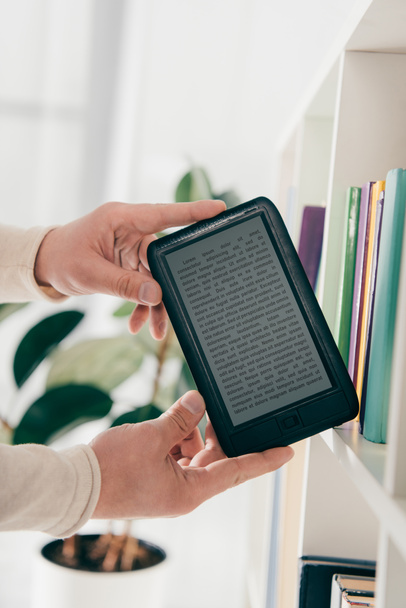 cropped view of man holding ebook in hands near bookshelf - Photo, Image