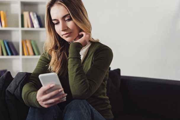 atraktivní žena držící smartphone zatímco sedí doma - Fotografie, Obrázek
