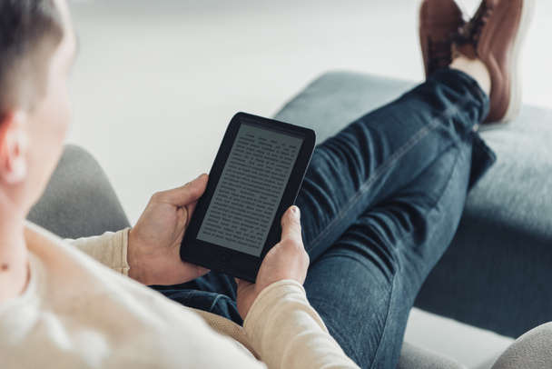 abgeschnittene Ansicht eines Mannes, der E-Books liest, während er zu Hause im Sessel sitzt - Foto, Bild