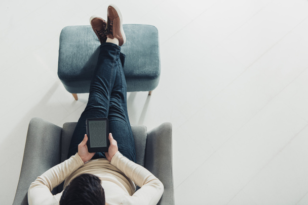 bovenaanzicht van man met e-reader zittend in fauteuil thuis - Foto, afbeelding