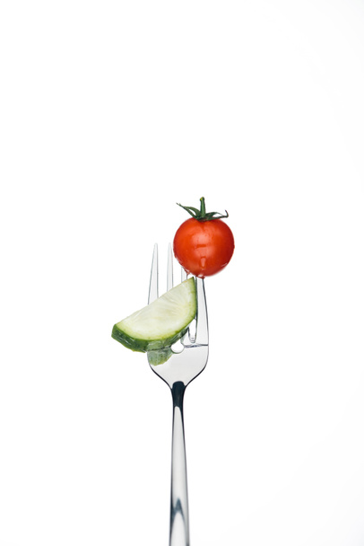 geheel rode cherry tomaat en een plakje komkommer op vork geïsoleerd op wit - Foto, afbeelding