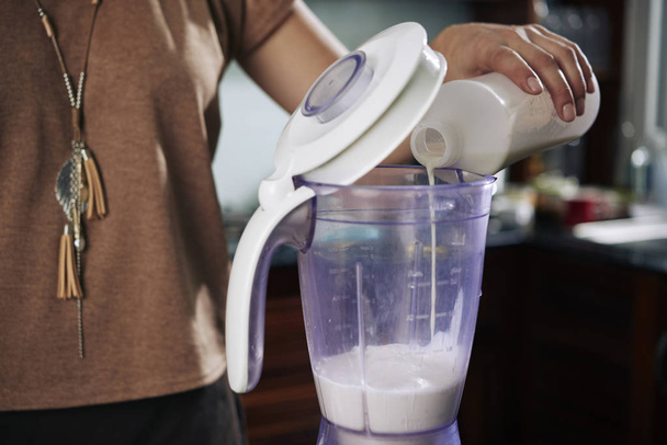 Hand der Person, die Milch in Mixer gießt, um köstlichen gesunden Cocktail zu machen - Foto, Bild