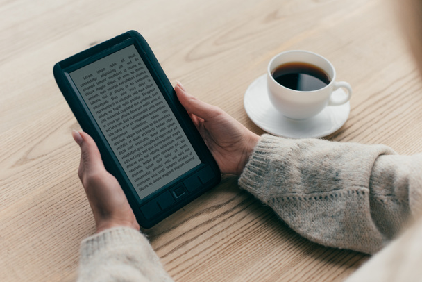 обрезанный вид женщины шипение с электронной книгой возле чашки кофе
 - Фото, изображение
