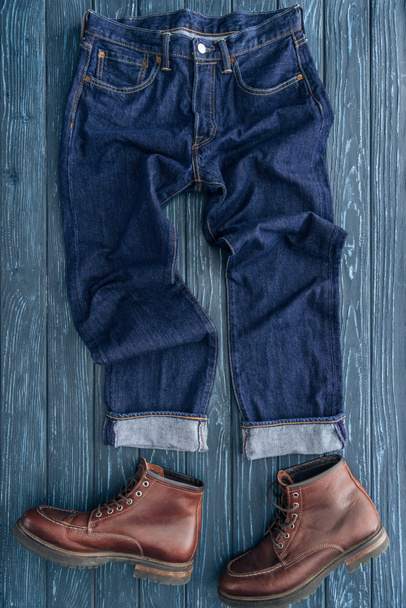 Top view of jeans and brown leather boots on wooden background - Foto, Imagen