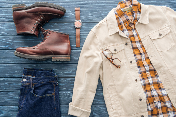 Flat lay with jeans, checkered shirt and leather boots on wooden background - Zdjęcie, obraz