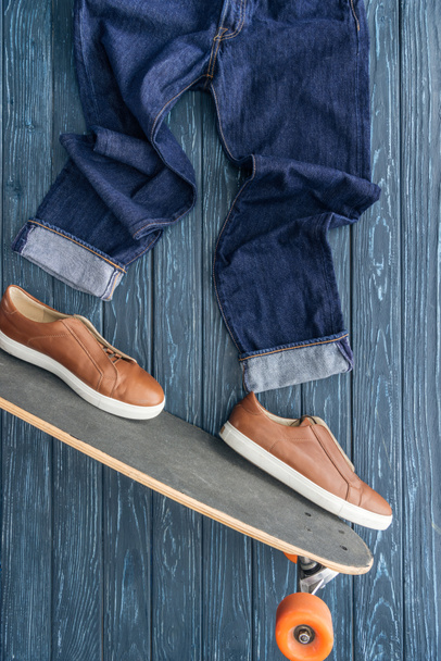 Top view of jeans, shoes and longboard on wooden background - Foto, afbeelding
