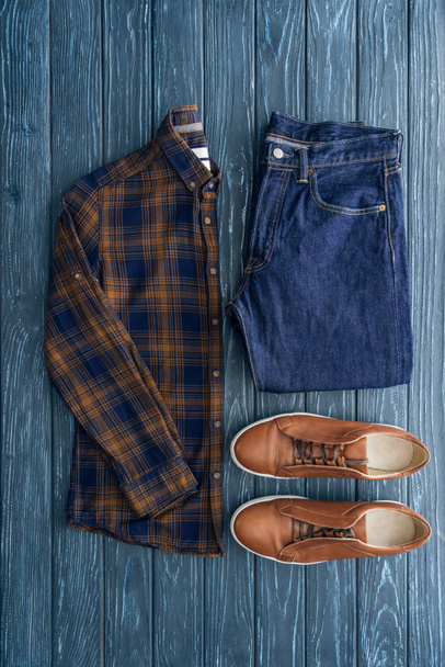 Top view of checkered shirt, jeans and brown shoes on wooden background - Fotografie, Obrázek