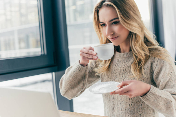 attraktive Frau lächelt, während sie Tasse mit Tee in der Hand hält - Foto, Bild