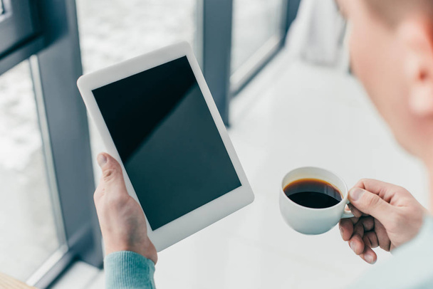 cropped view of man holding cup with coffee and digital tablet with blank screen in hands - Фото, изображение