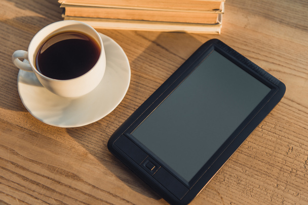 black e-reader with blank screen lying near cup with coffee on table  - Foto, Imagen