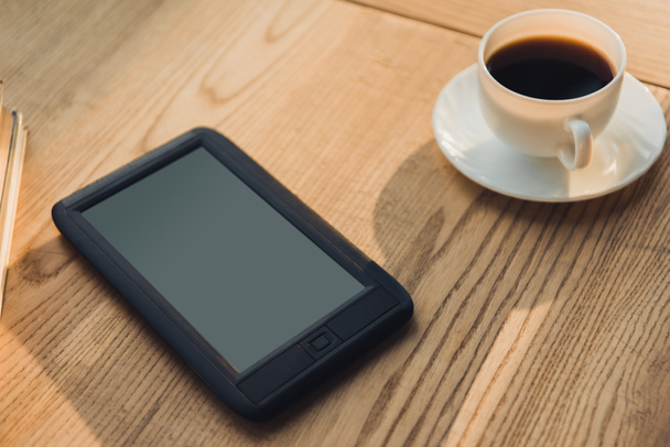eBook mit leerem Bildschirm neben Tasse mit Kaffee liegend  - Foto, Bild