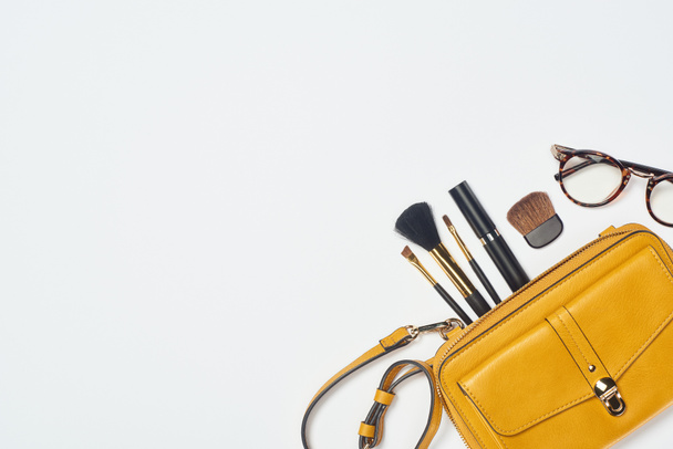 Gafas, rímel, cepillos cosméticos y bolsa amarilla sobre fondo blanco
 - Foto, Imagen