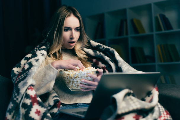 σοκαρισμένος γυναίκα βλέποντας ταινία για φορητό υπολογιστή και κρατώντας μπολ με ποπ-κορν - Φωτογραφία, εικόνα