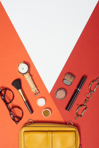 Flat lay with mascara, watch, yellow bag, bracelet, eyeshadow, blush, glasses and cosmetic brushes - 写真・画像