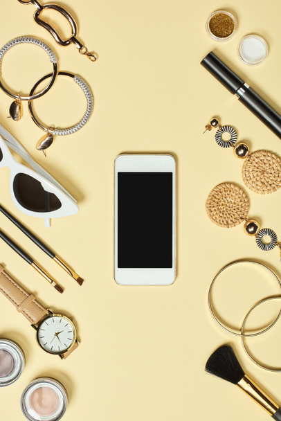 Top view of watch, bracelets, earrings, sunglasses, eyeshadow, blush, cosmetic brushes, mascara and smartphone with copy space - Foto, Imagen