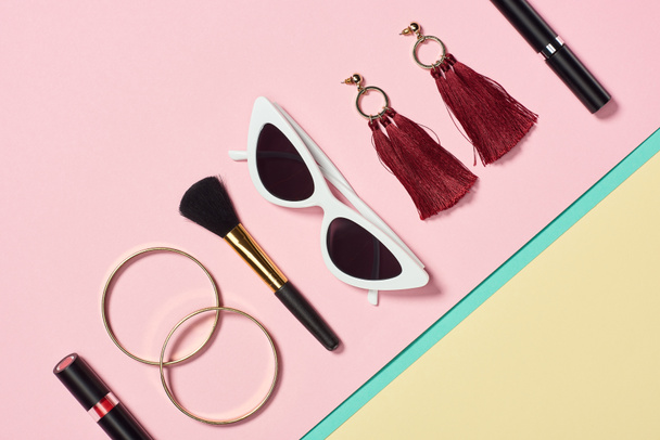 Flat lay with lipstick, bracelets, earrings, cosmetic brush, sunglasses and mascara - 写真・画像