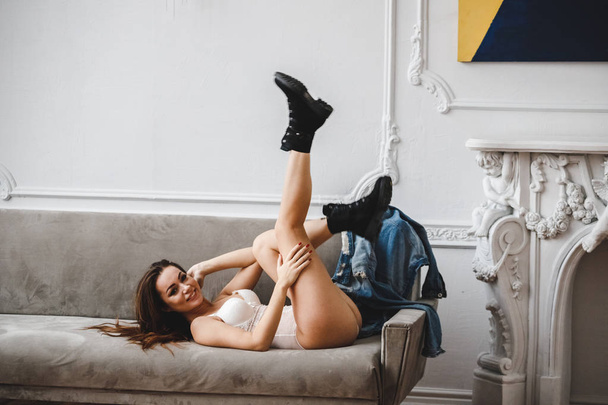 Beauty brunette woman in white lingerie posing on sofa at luxury apartments interior   - 写真・画像