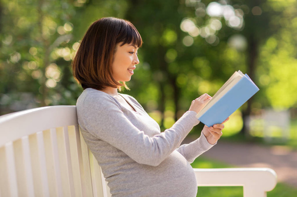 happy pregnant asian woman reading book at park - 写真・画像