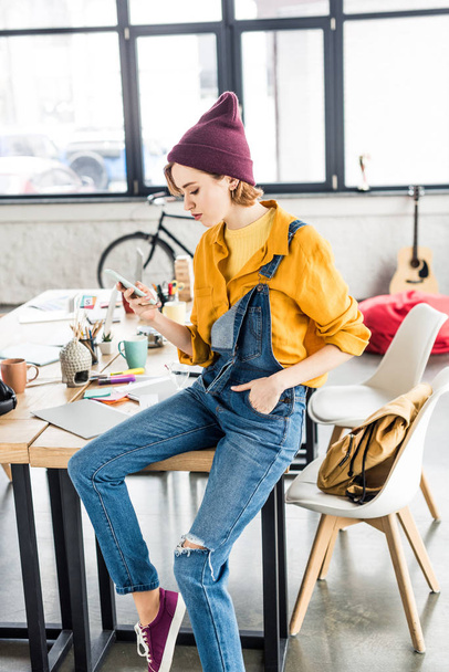 female designer sitting on table and using smartphone in loft office - Photo, Image