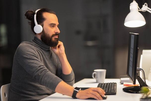 creative man in headphones working at night office - Foto, Bild