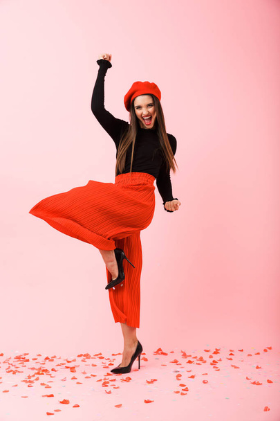 Full length portrait of a beautiful young woman wearing red beret standing isolated over pink background, success - Zdjęcie, obraz