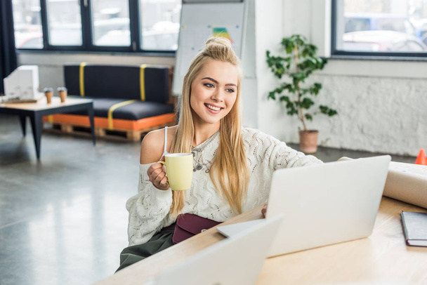 casual businesswoman sitting at computer desk with cup of coffee in loft office - Valokuva, kuva