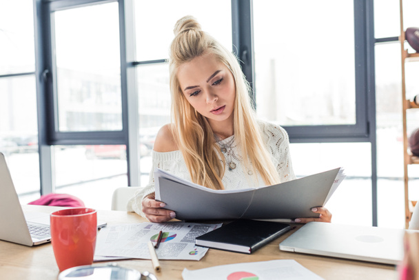 beautiful casual businesswoman sitting at desk and holding document in loft office - Foto, Bild