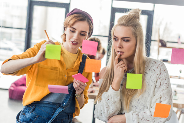 beautiful casual businesswomen looking at colorful sticky notes on glass window in office - Fotografie, Obrázek