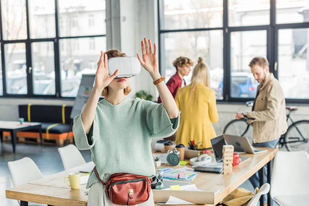 female designer gesturing with hands while having virtual reality experience in loft office with colleagues on background - Fotó, kép