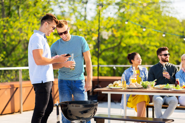 happy friends grilling at bbq party on rooftop - Foto, Bild