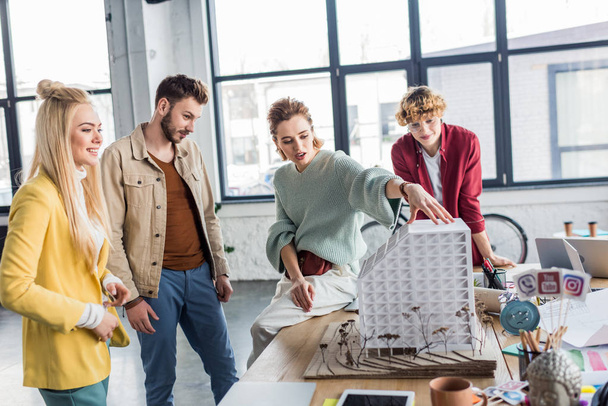 группа женщин и мужчин-архитекторов, работающих вместе над моделью дома в лофт-офисе
 - Фото, изображение