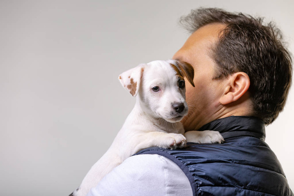 Horizontal portrait of handsome cheerful man holds jack russell terrirer, has glad expression - Photo, Image