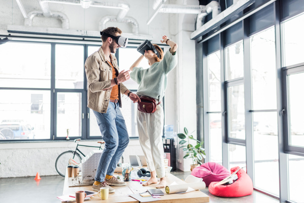 female and male designers wearing vr headset, gesturing with hands and having virtual reality experience in loft office - Foto, afbeelding