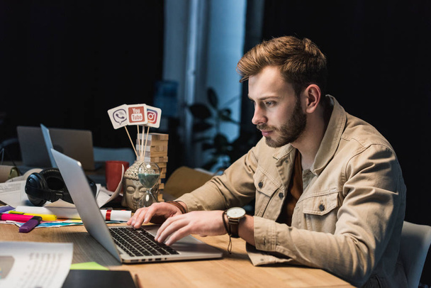 handsome casual businessman sitting at table and using laptop in office - Valokuva, kuva