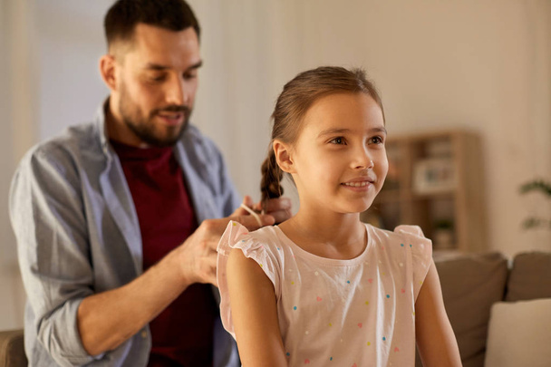 father braiding daughter hair at home - Foto, afbeelding